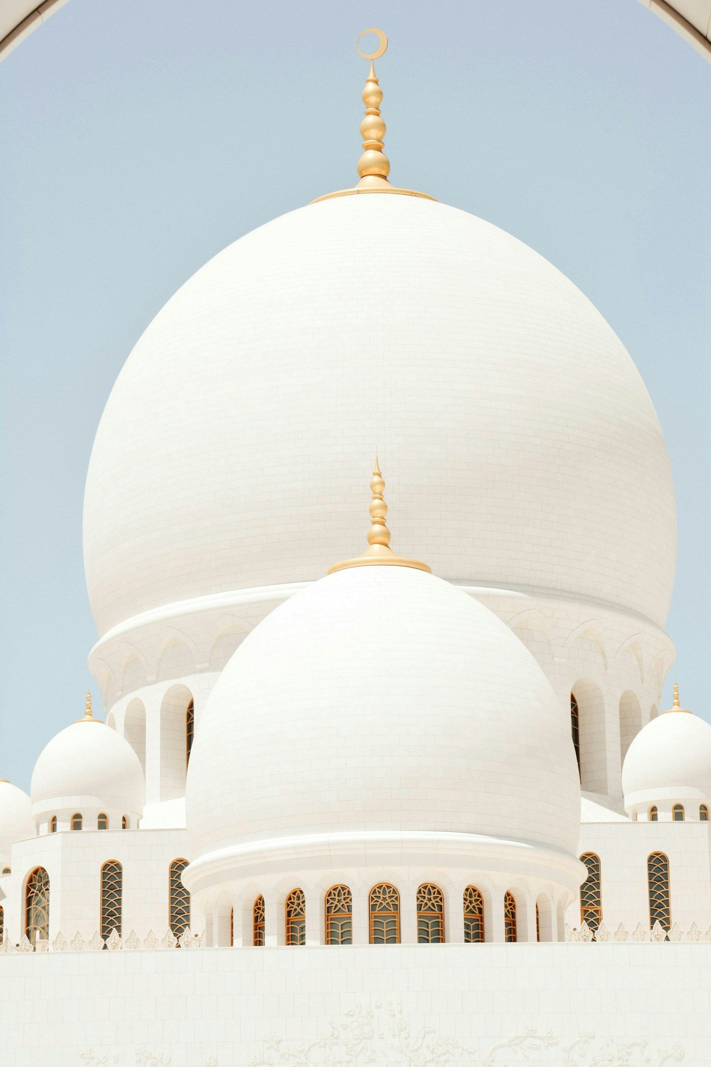 White mosque domes with golden finials against a pale sky